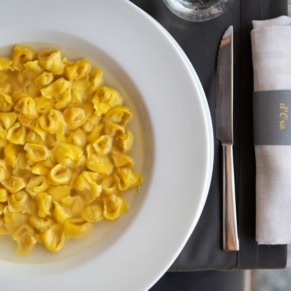 A plate of tortellini in broth next to a neatly set table with a knife and napkin.