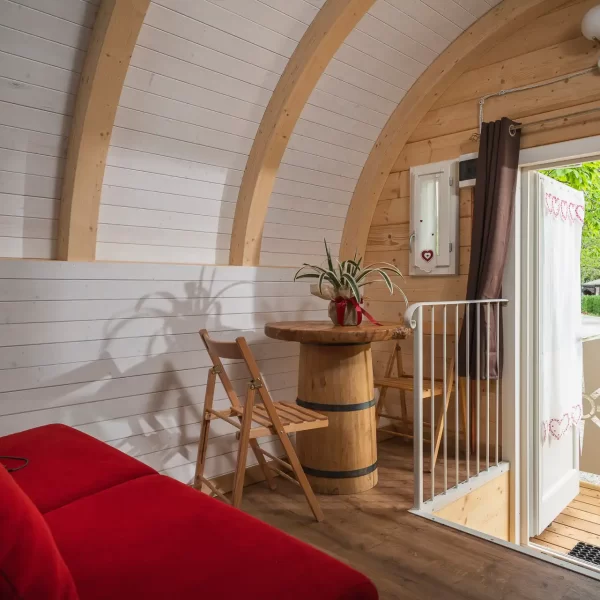 Gemütlicher Innenraum einer Holzhütte mit roten Polstermöbeln und offen stehender Tür zur Terrasse.
